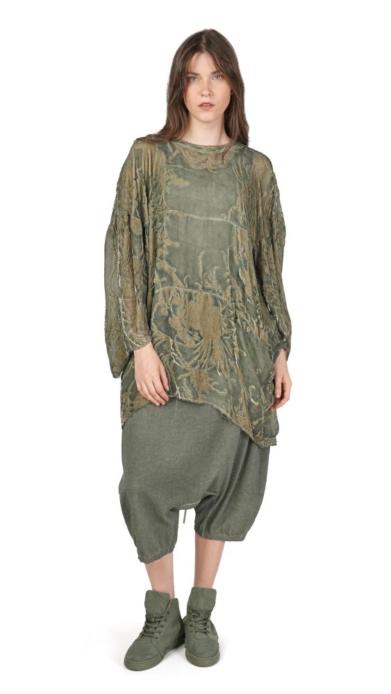 Frau trägt oversized grünes Kleid mit asymmetrischen Ärmeln und weiten Hosen, kombiniert mit grünen Stiefeln.
