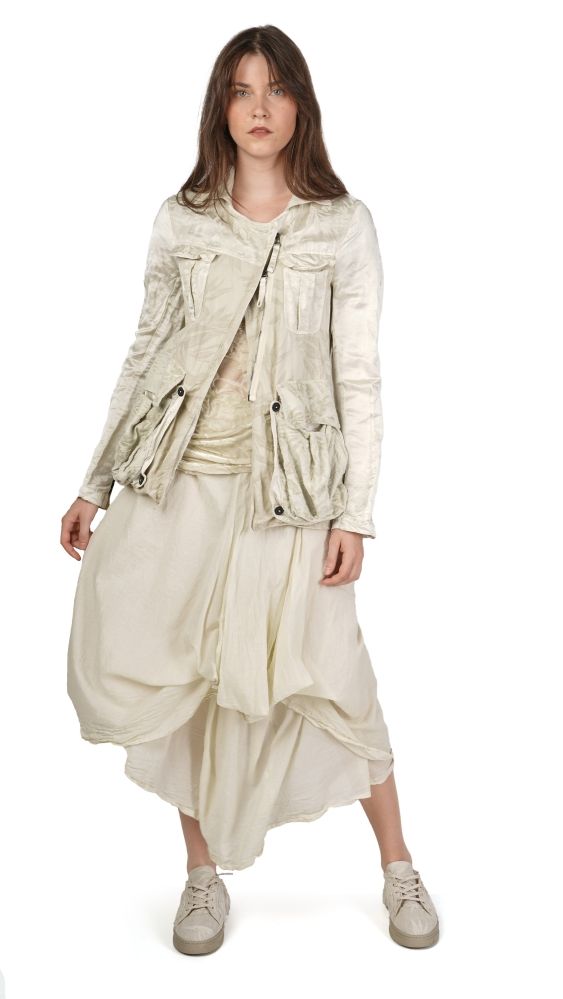 Frau trägt oversized beige Jacke mit Asymmetrie und weitem, zerknittertem Rock, barfuß mit Sneakern.