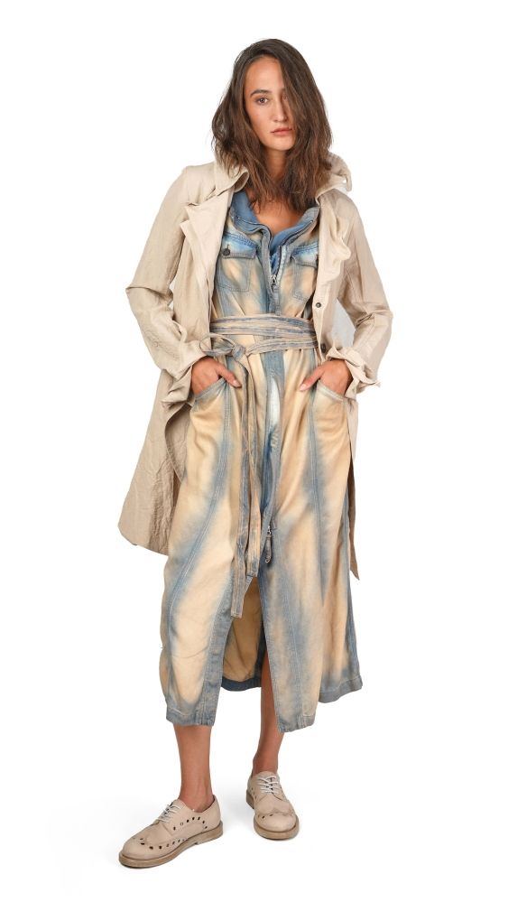 Frau trägt lange beige Jacke über blauem Denim-Kleid mit Gürtel, weiße Sneakers.