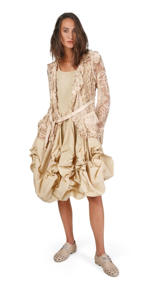 Frau trägt bohemisches, langes Kleid mit Rüschen und durchsichtigem Jackett, beige, mit Sandalen.