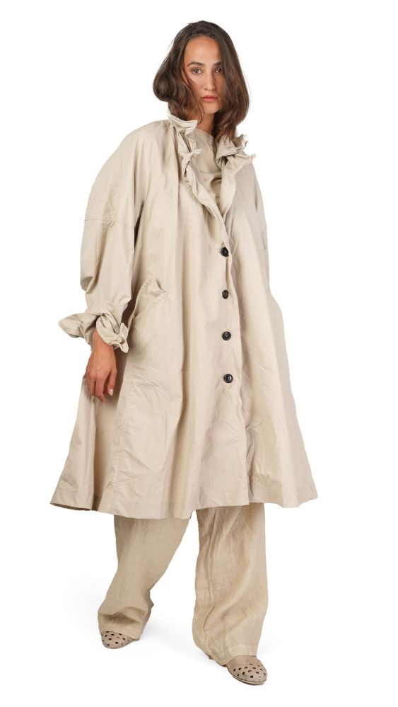Vintage-Look: Frau in beige Überwurfkleid mit weitem Schnitt und passenden Hosen, barfuß auf hellen Untergrund.