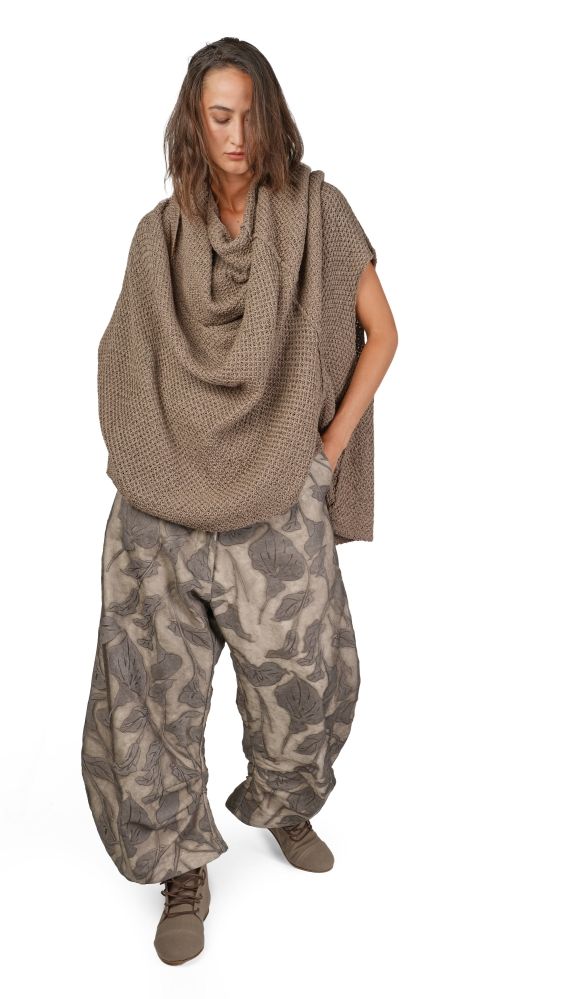 Frau trägt oversized Strickponcho mit weitem Musterhosenlook und robusten Stiefeln.