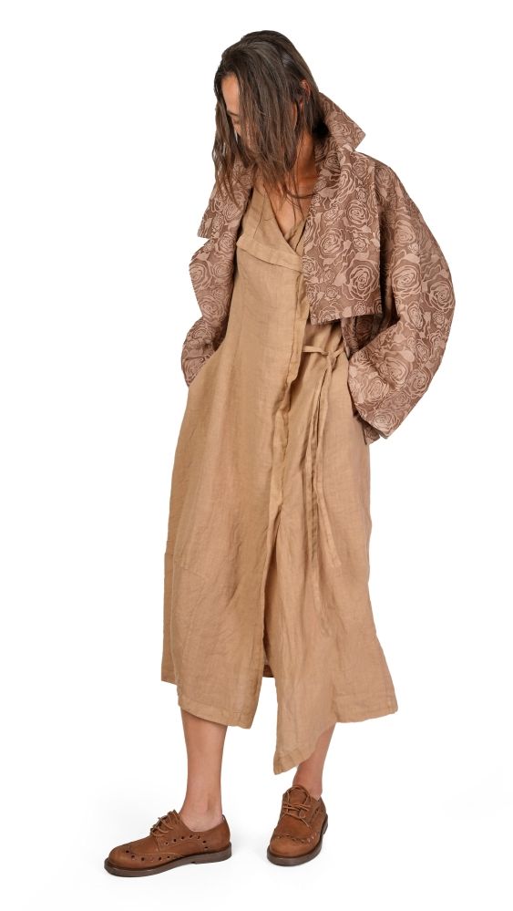 Person trägt langes beige Gewand mit Muster-Jacke und braunen Schuhen, lässig drapiert.