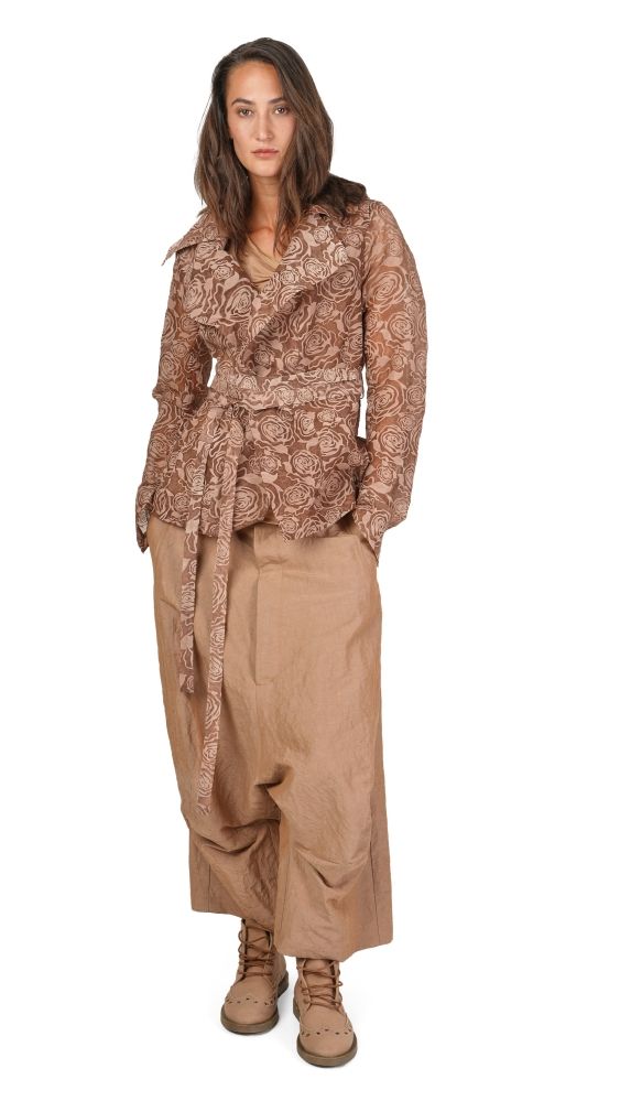 Frau trägt beige, langes Kleid mit Stickmuster-Bluse und weiten Hosen, kombiniert mit robusten Stiefeln.