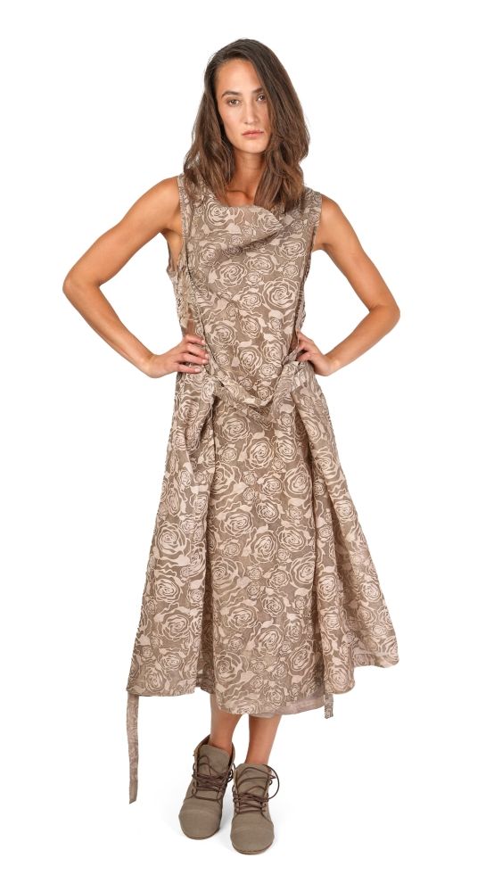 Frau trägt langes, gemustertes Kleid mit Schlitz und bequemen Schuhen, Hände in Hüften gestützt.