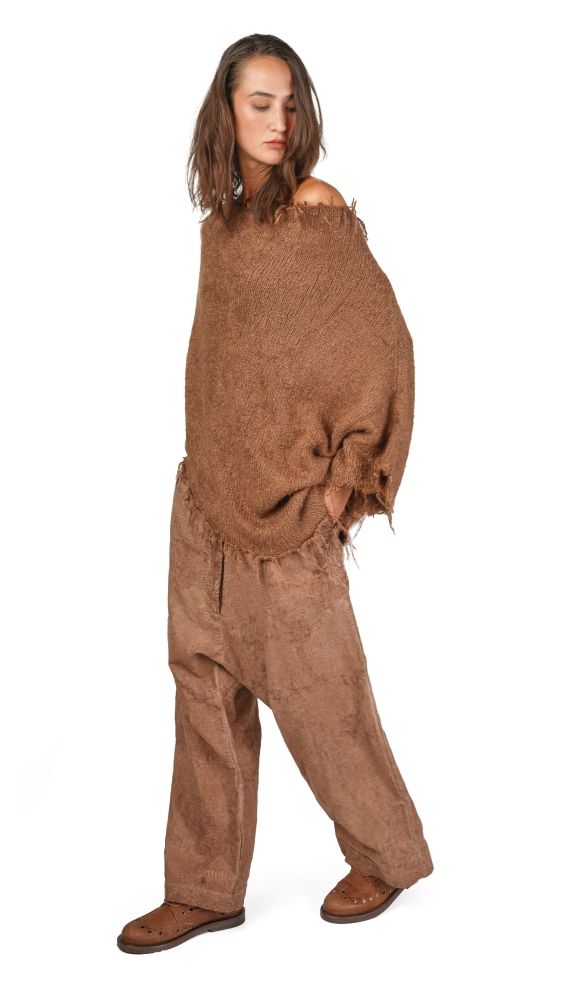 Person trägt beigefarbenes, zerrissenes Overall-Kleid mit Fransen und flachen Schuhen.
