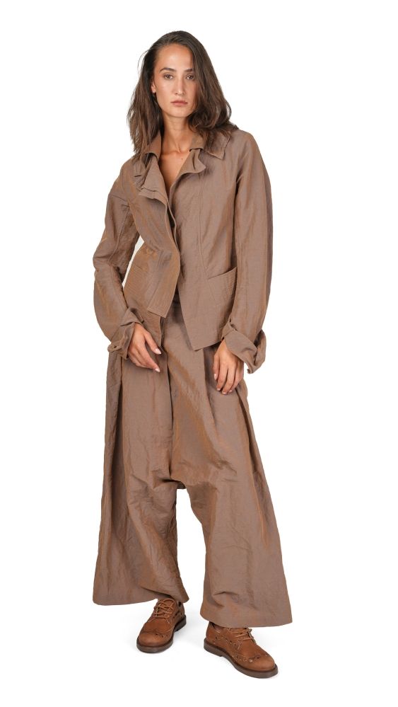 Frau trägt oversized beige Jumpsuit mit weitem Schnitt und braunen Stiefeln.