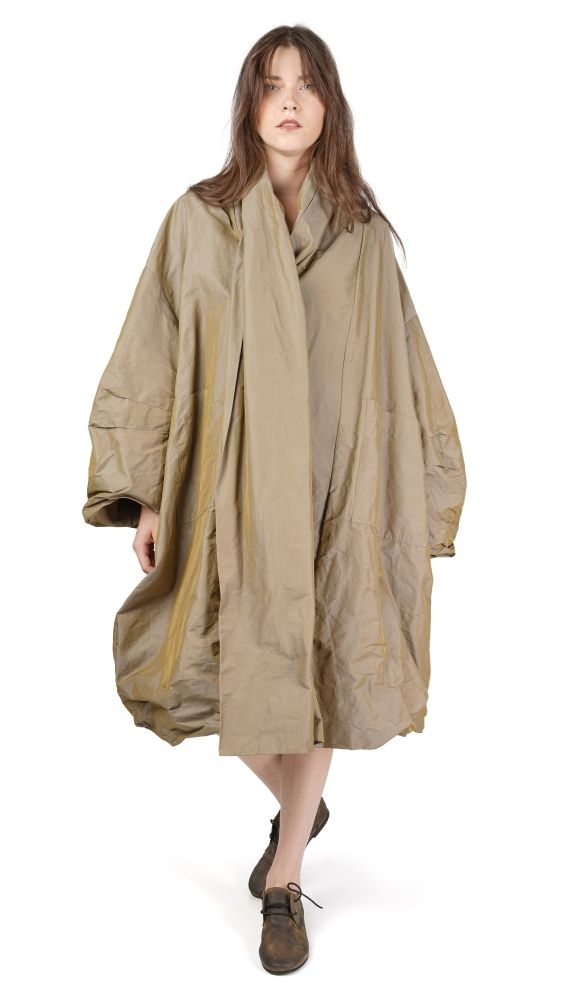 Person trägt oversized, beigefarbenen Mantel mit weitem Schnitt und flachen Schuhen.