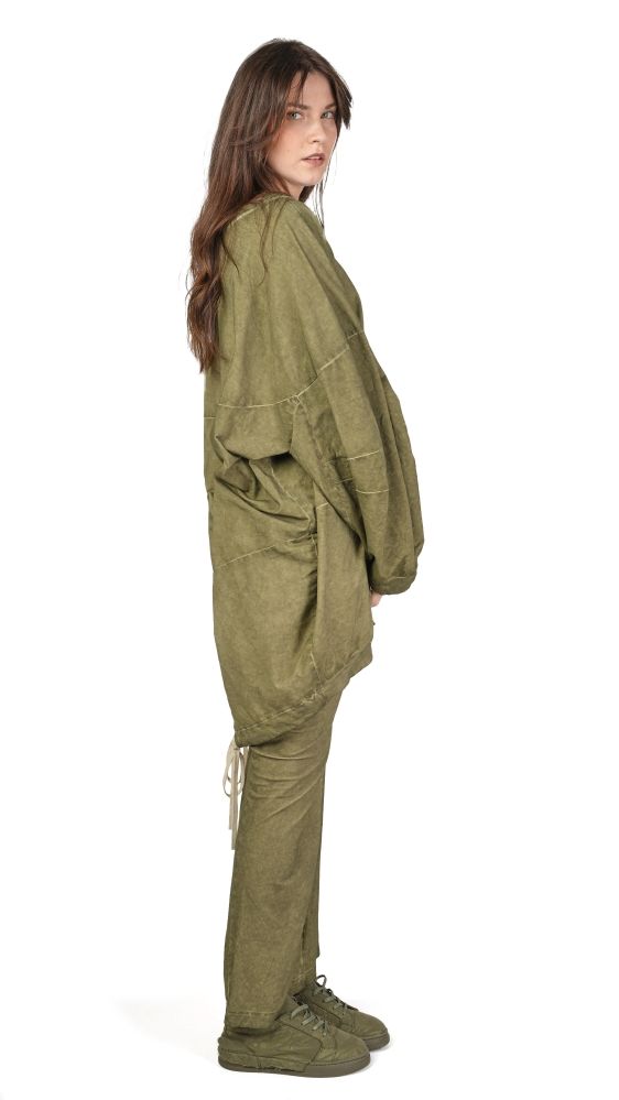 Person trägt olivgrünen Overall mit weitem Schnitt und robusten Schuhen, seitliches Profilansicht.