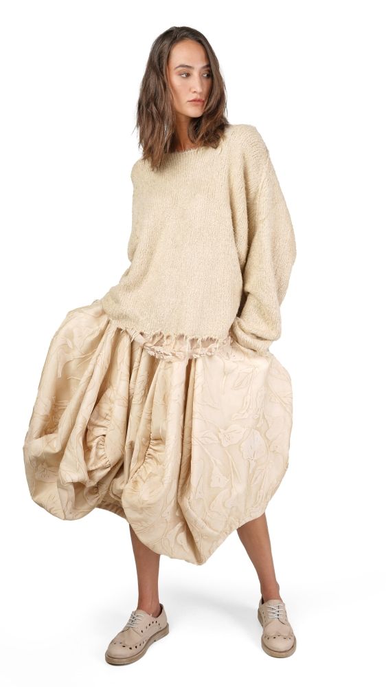 Frau trägt cremefarbenen oversized Pullover mit weitem, gemustertem Rock und Sneakern.