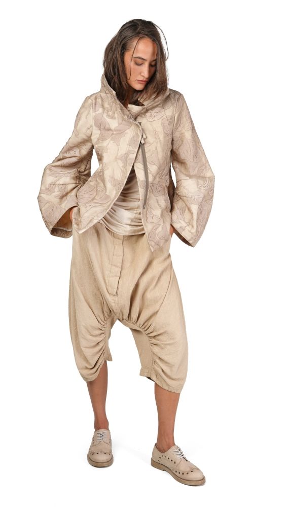 Person trägt beige, oversized Jacke mit Muster, weite Haremhose und Sneaker, lässige Pose.