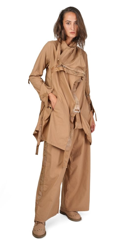 Frau trägt beiges, weit geschnittenes Überwurfkleid mit weiten Hosen und flachen Schuhen.