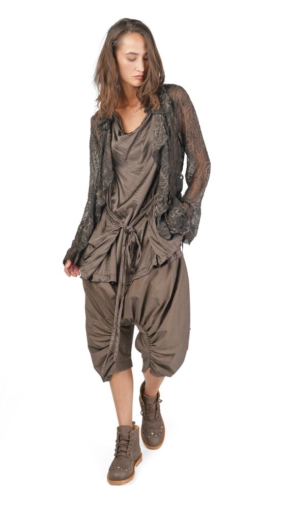 Frau trägt bohemisches, langes Kleid mit durchsichtigen Ärmeln und weiten Hosen, kombiniert mit robusten Stiefeln.